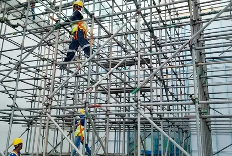 Construction workers wearing safety helmets and harnesses working on multi-level metal scaffolding.