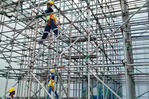 Construction workers wearing safety helmets and harnesses working on multi-level metal scaffolding.