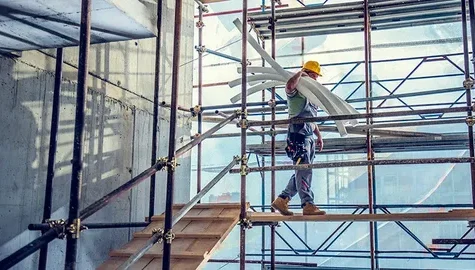 Construction worker carrying pipes on scaffolding inside a building under construction