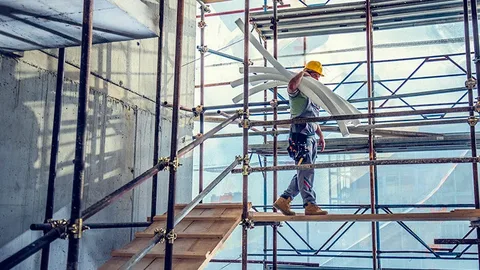Construction worker carrying pipes on scaffolding inside a building under construction