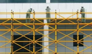 Workers standing on yellow scaffolding structure at a commercial building site