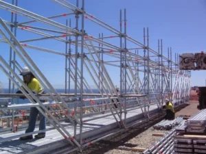 Workers assembling large metal scaffolding structure outdoors.