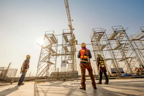 Construction workers in safety gear standing near scaffolding structure.