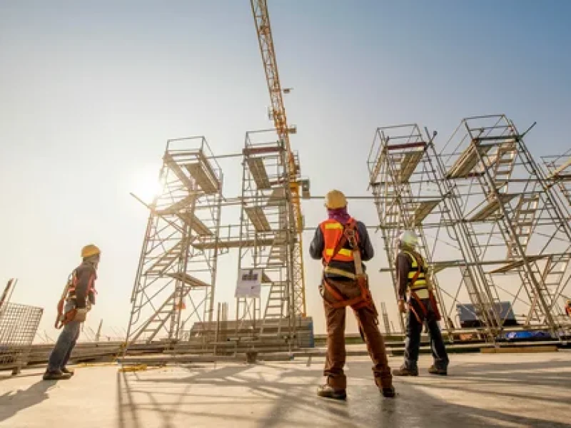 Construction workers in safety gear standing near scaffolding structure.